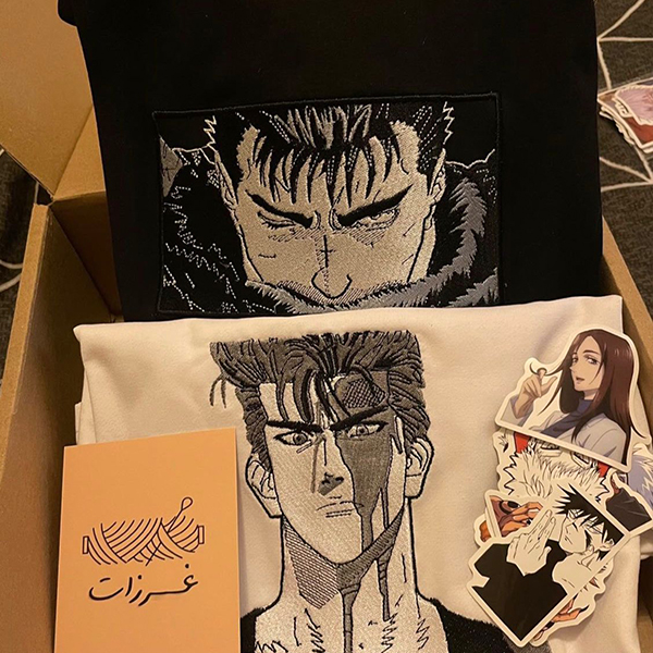 Assorted anime-themed merchandise including t-shirts, stickers, and a card with intricate designs